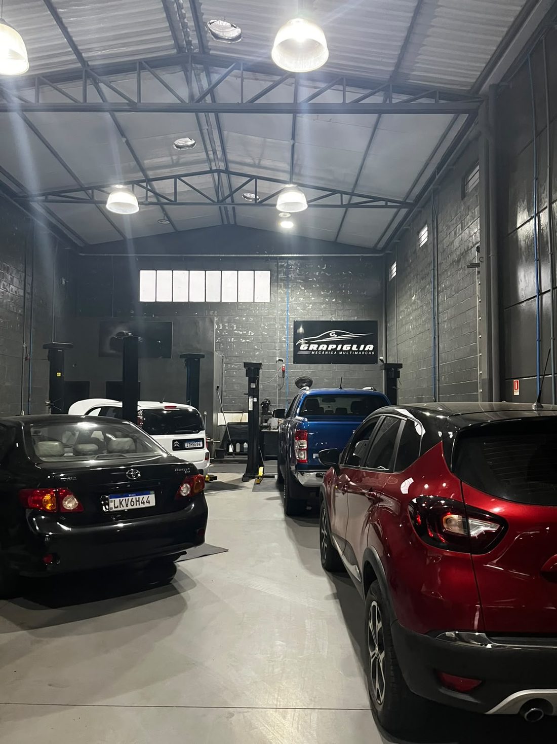 Carros nos boxes de serviço da Grapiglia, com elevadores e painel da marca ao fundo